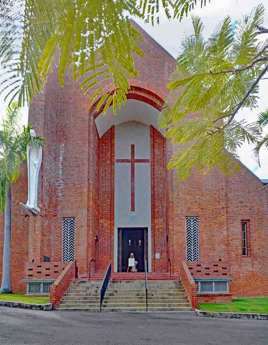 The west front of St James’ Cathedral: red brick, a tall cross above the door, and the statue of St James among the trees.